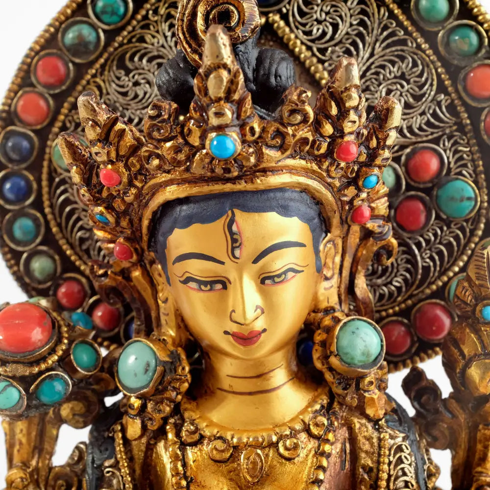 Das anmutige Gesicht der Weißen Tara Statue ist in Gold gefasst, ihre Augen blicken entspannt. Auf ihrer rechten Schulter ist eine voll erblühte Lotusblume, auf der linken Schulter eine Knospe. 