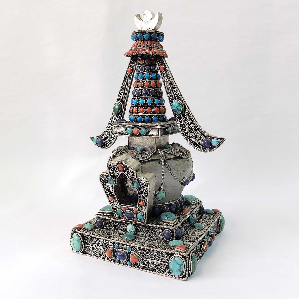 Stupa aus Kupfer, mit Filigran verziert, versilbert, mit Türkis, Koralle und Lapislazuli besetzt. Die Kuppel ist aus Kristall. 